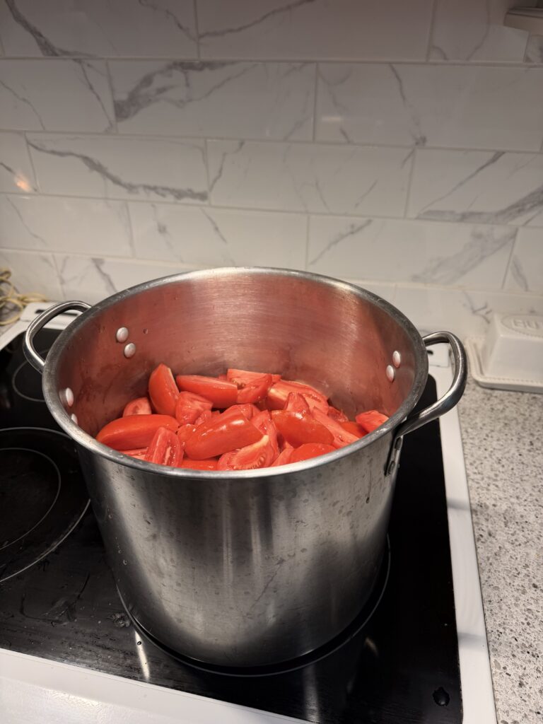 Large stainless-steel stockpot filled with peeled Roma tomatoes ready to be cooked for homemade tomato sauce.